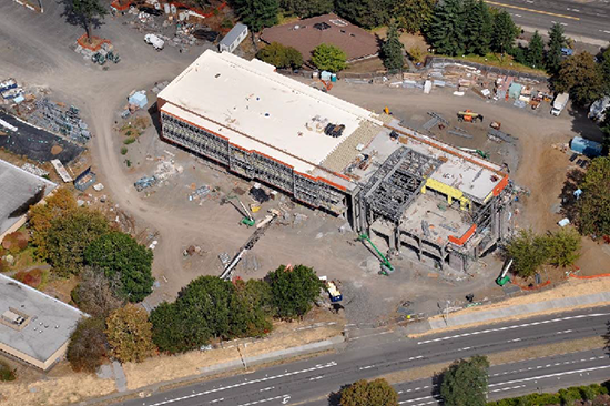 This September 5, 2015, aerial shot shows the roof covering about two-thirds complete. The remainder of the roof will be installed once all of the heavy structural work and welding are completed at the high roof. The gray structural elements of the lobby and high roof can be seen toward the right (east) end of the building. Photo by Skanska 