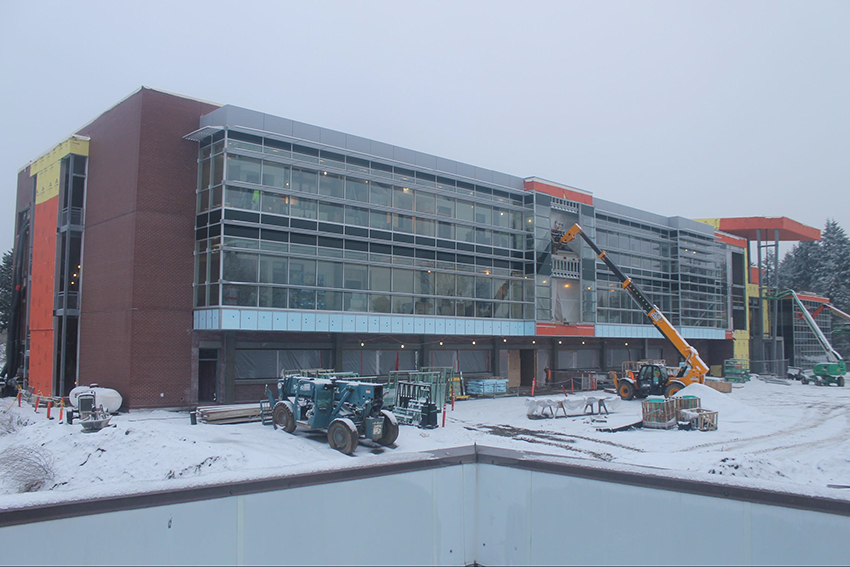 South facing facade. Entrance is the orange canopy area on far right. The lift is delivering materials to the 3rd and 4th floors.