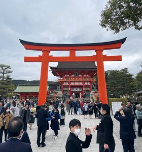 A giant orange torii gate in front of the Romon Gate at the Fushimi Inari Shrine entrance in Kyoto, Japan.